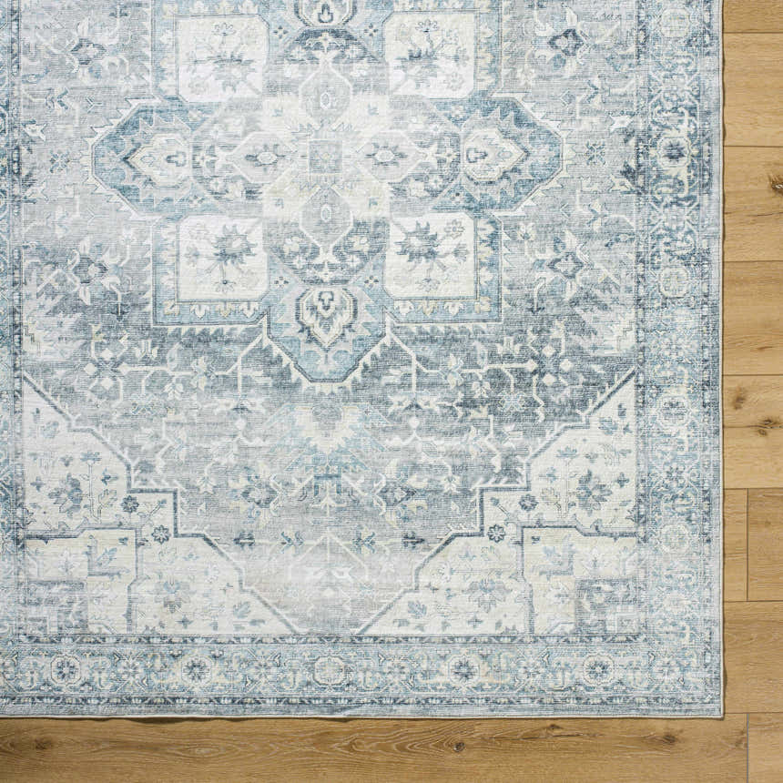 Close-up of the Mauro Blue Medallion Washable Area Rug showing its traditional light gray, silver, and blue pattern. Corner