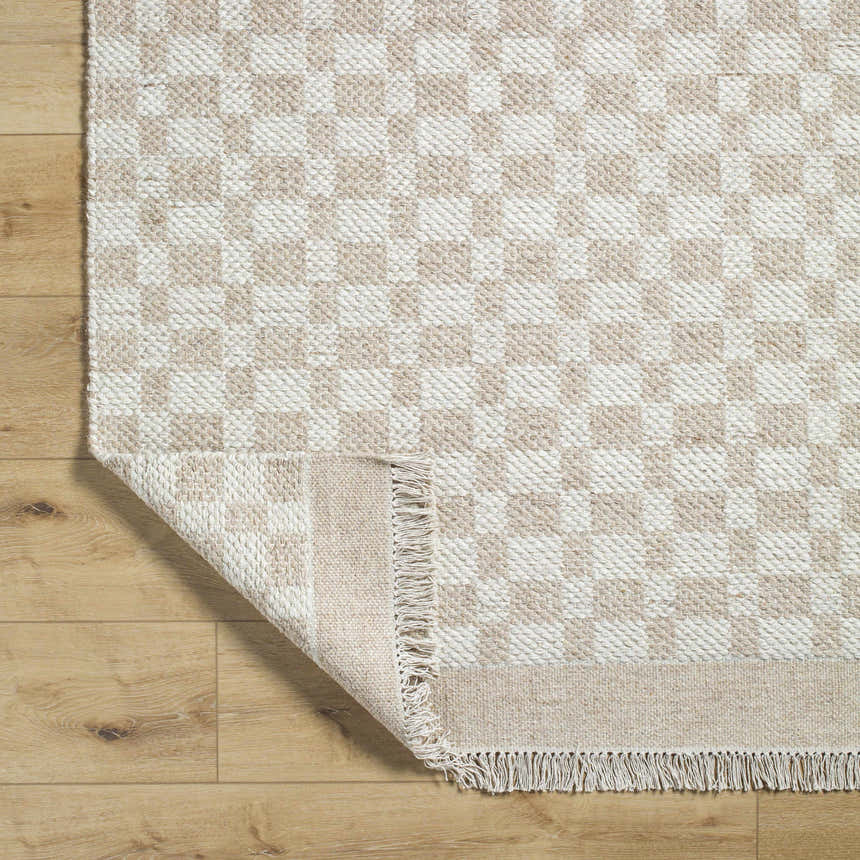 Close-up of the hand-woven Meira Tan Area Rug showing its ivory and tan checkered pattern and tasseled edge. Fold