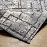 Close-up of the Mace Area Rug, showcasing its charcoal, cream, and slate colors and geometric pattern. Fold