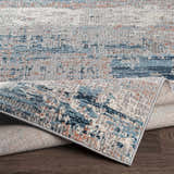 Close-up of McCracken Area Rug showing abstract blue, gray, and peach pattern and textured weave. Fold