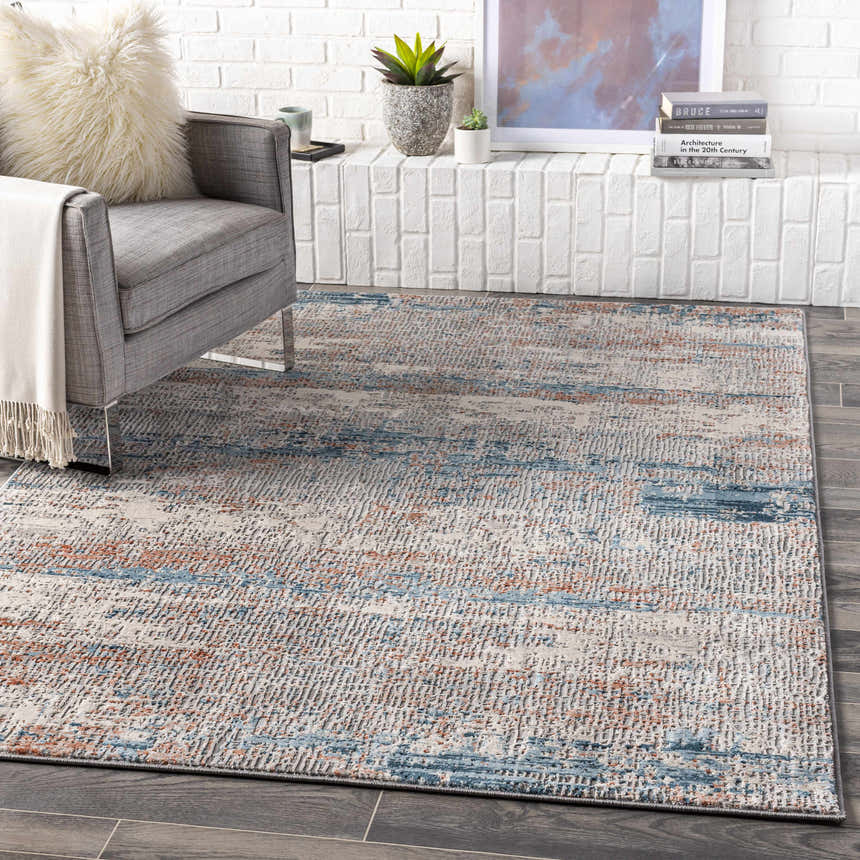 Living room scene with a gray chair and the McCracken Area Rug in blue and orange tones. Roomscene-Rectangle