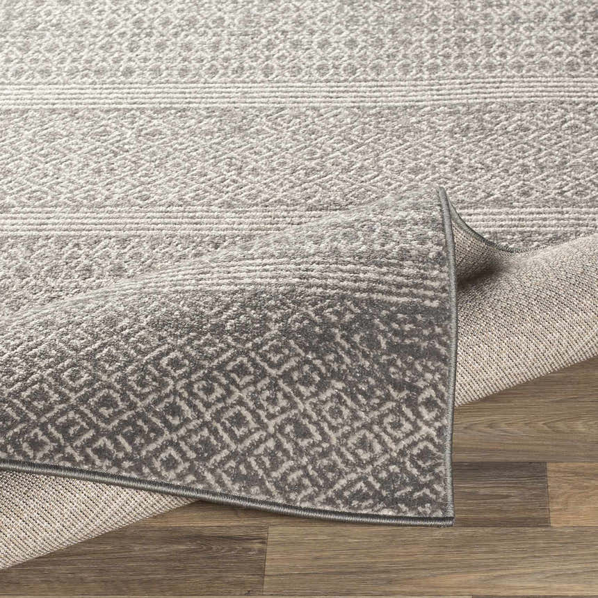 Close-up of the Mckinney Area Rug. Charcoal, light beige, and gray geometric pattern. Machine woven texture. Fold