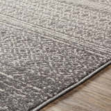 Close-up of the Mckinney Area Rug. Charcoal, light beige, and gray tones with a subtle geometric pattern. Machine woven texture. Texture