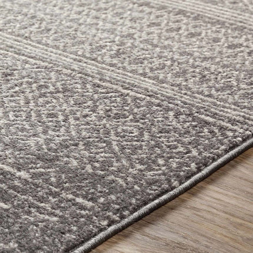 Close-up of the Mckinney Area Rug. Charcoal, light beige, and gray tones with a subtle geometric pattern. Machine woven texture. Texture
