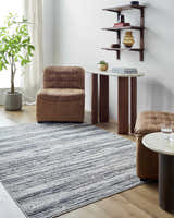Living room scene with a Munya Area Rug in charcoal, cream, and gray, paired with leather furniture and wood accents. Roomscene-Rectangle