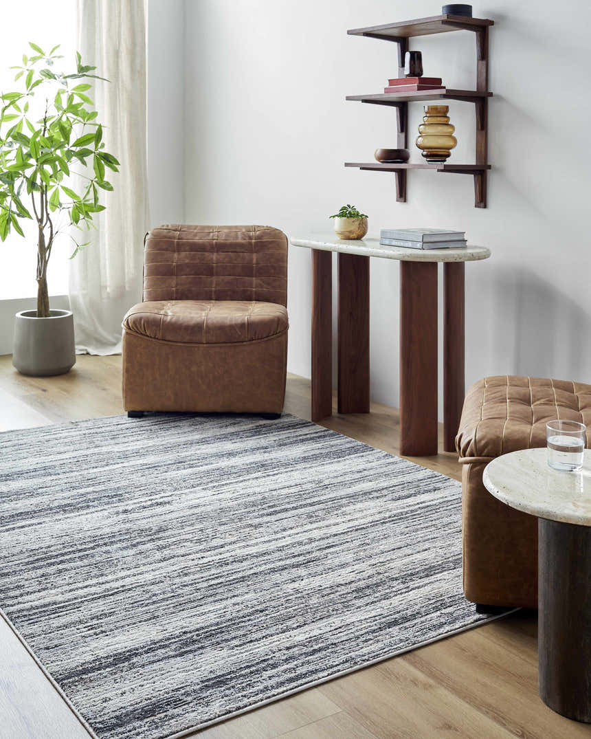 Living room scene with a Munya Area Rug in charcoal, cream, and gray, paired with leather furniture and wood accents. Roomscene-Rectangle