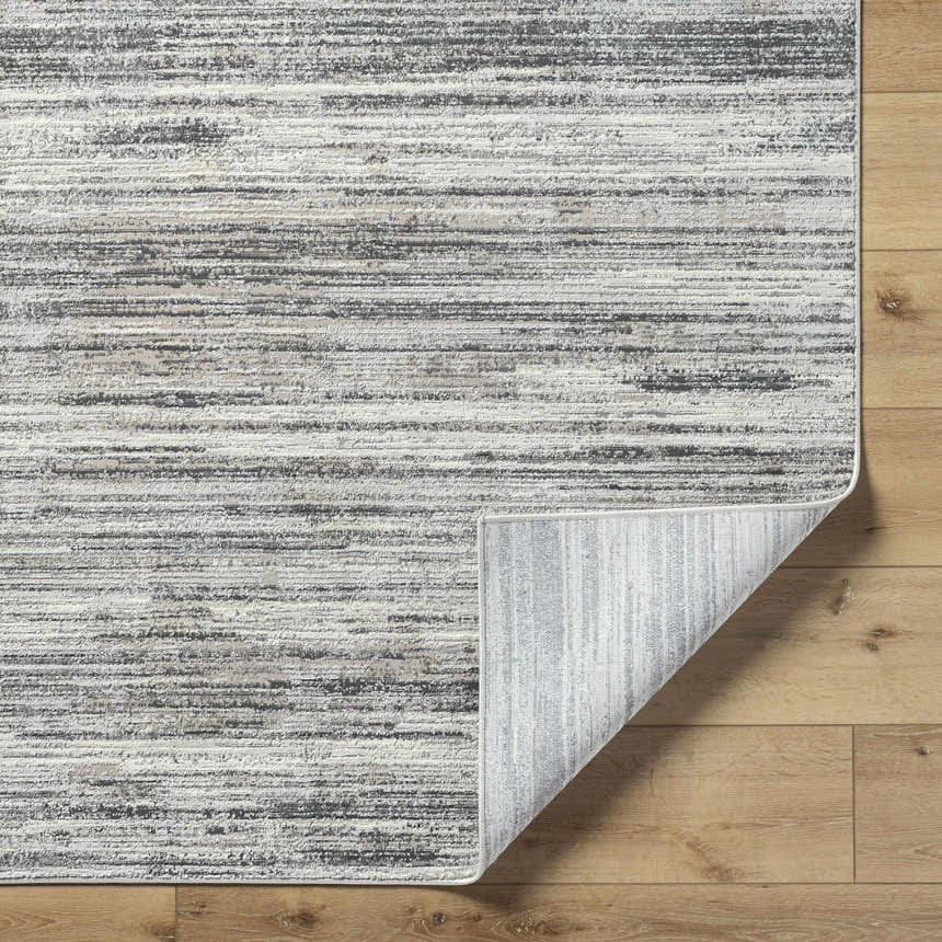Close-up of the Munya Area Rug showing charcoal, cream, and gray horizontal stripes on a wood floor. Rug corner is folded. Fold