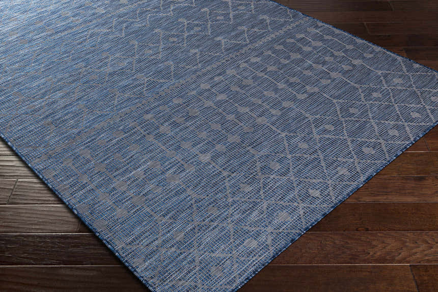 Close-up of Maddingley Flatweave Area Carpet in blue and dark blue with a geometric pattern on dark wood flooring. Corner