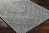 Close-up of a hand-tufted Wool Texture Area Rug in black and cream with a geometric square pattern on dark wood floors. Corner