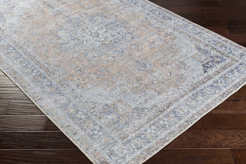 Close-up of the Mianay Washable Area Rug showing its beige, blue, and light gray vintage-style pattern on dark wood flooring. Corner