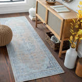 Entryway scene with a beige and blue Mianay Washable Area Rug, wood console table, pouf, and dark wood floors. Roomscene-Runner