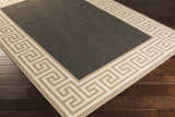Close-up of the Michael Area Rug: a gray rug with a Greek key pattern border in beige and cream on dark wood floors. Corner