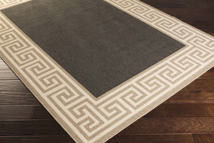 Close-up of the Michael Area Rug: a gray rug with a Greek key pattern border in beige and cream on dark wood floors. Corner