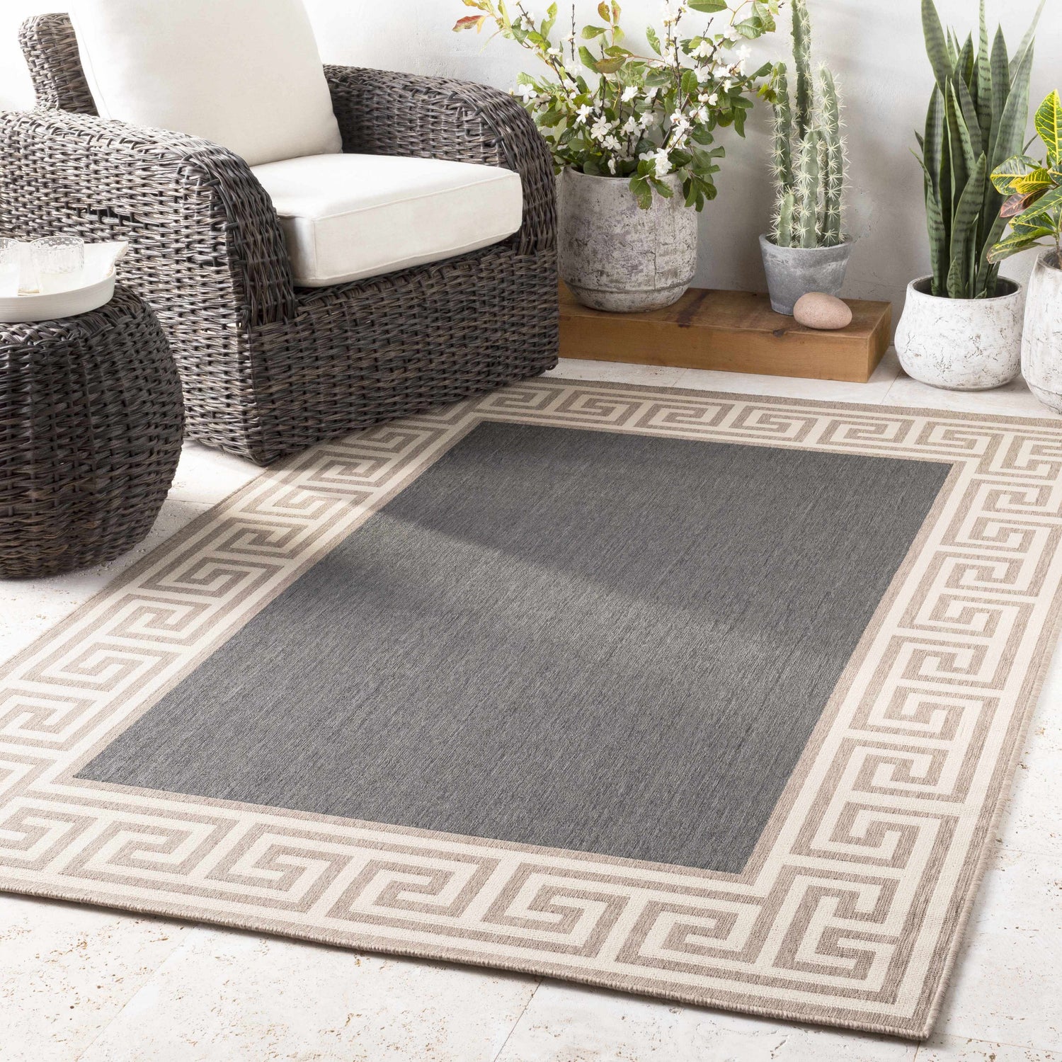 Outdoor patio scene with a gray Michael Area Rug featuring a Greek key border, plus wicker furniture and potted plants. Roomscene-Rectangle