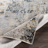 Close-up of the Midfield Luxe Rug showing its charcoal, cream, gray, and teal contemporary pattern and soft polyester texture. Fold