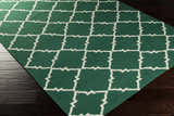 Close-up of the Minehead Area Rug. Dark green wool rug with a light gray geometric trellis pattern on dark wood floors. Corner