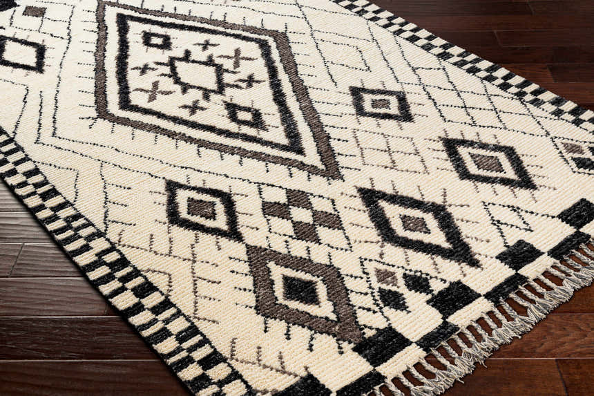 Close-up of the hand-knotted Minyama Area Rug. Cream wool with black and charcoal geometric diamond pattern and checkered fringe. Corner