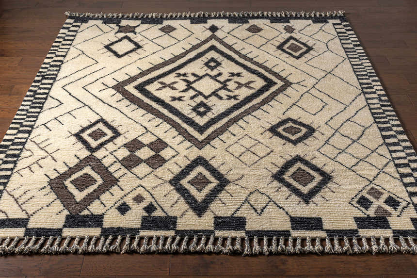 Close-up of the Minyama Area Rug showcasing its cream base, black and charcoal geometric pattern, and hand-knotted fringe. Front