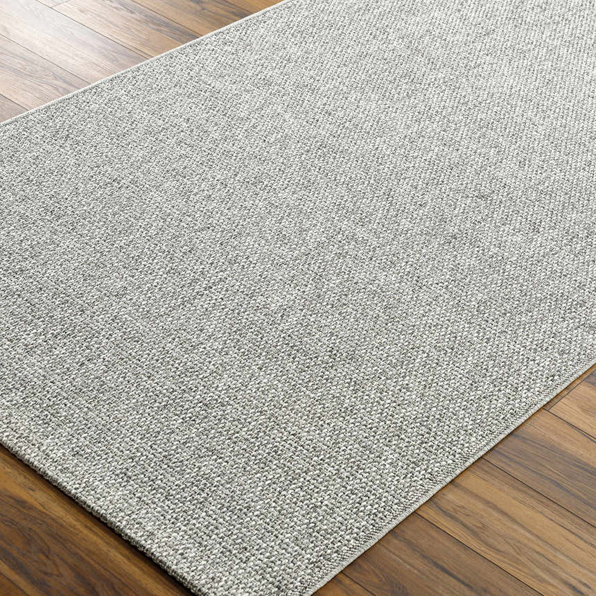 Close-up of the Medih Area Rug showing its gray woven texture and pattern on a wood floor. Corner