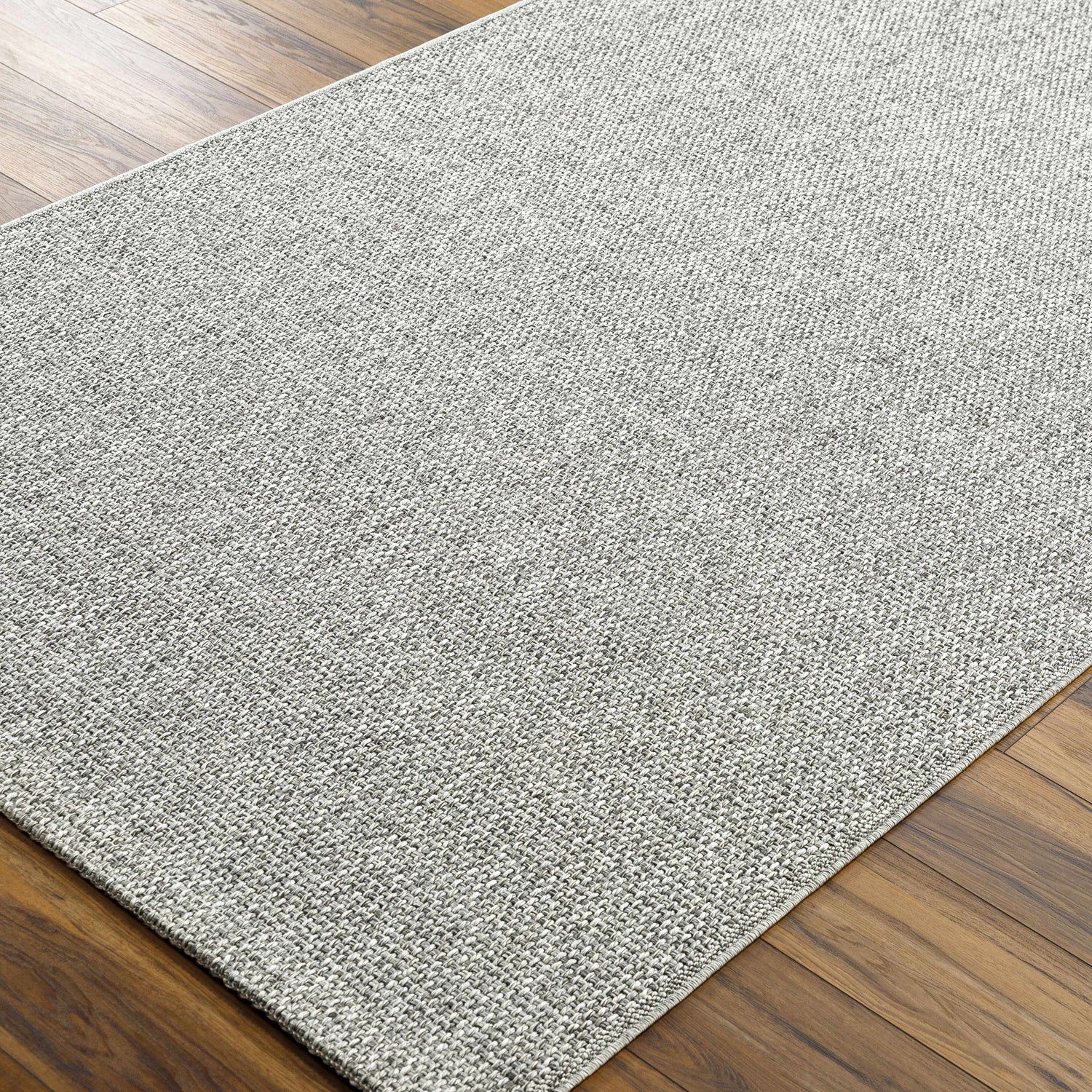 Close-up of the Medih Area Rug showing its gray woven texture and pattern on a wood floor. Corner