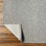 Close-up of the gray Medih Area Rug showing its woven texture and backing on a wood floor. Fold