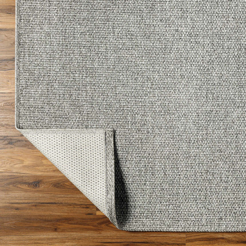 Close-up of the gray Medih Area Rug showing its woven texture and backing on a wood floor. Fold