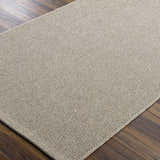 Close-up of the woven texture and neutral beige color of the Matah Beige Outdoor Area Rug on a dark wood floor. Corner