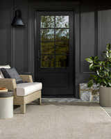 Outdoor patio scene with a Matah Beige Outdoor Area Rug, chair, and potted plant against a dark gray exterior. Roomscene-Rectangle