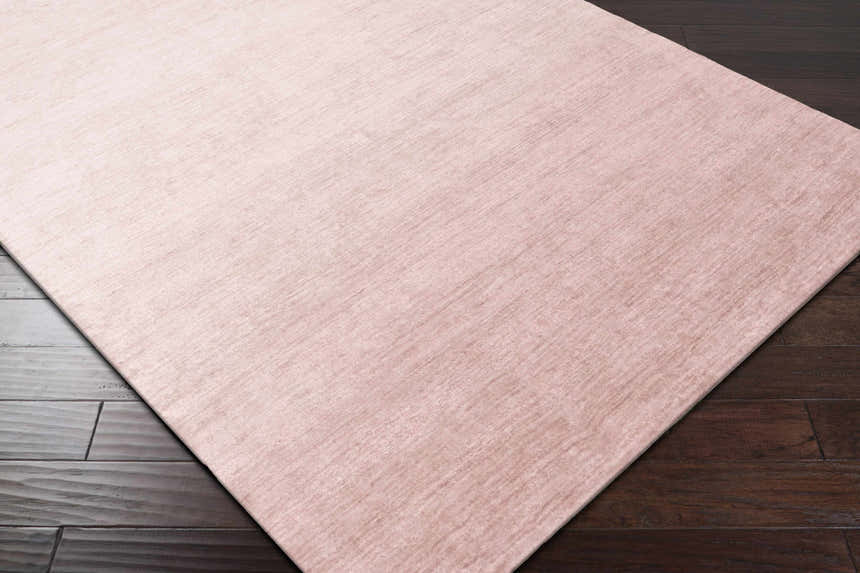 Close-up of the hand-loomed Millinocket Area Rug in dusty pink, showing its subtle texture on dark wood floors. Corner