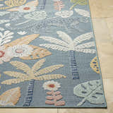 Close-up of the Micha Area Rug. Features a blue background with a floral and palm tree pattern in cream, mustard, and olive tones. Front