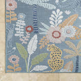 Close-up of the Micha Area Rug. Blue rug with floral, palm tree, and leopard pattern in cream, mustard, olive, and rust. Corner