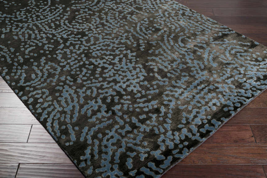 Close-up of the Pensacola Denim/Black rug showing its abstract denim blue pattern on a dark charcoal background. Corner