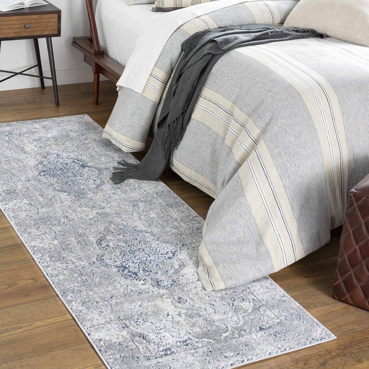 Bedroom scene with a gray and navy Mountsorrel Area Rug next to a bed with striped bedding and a gray throw. Roomscene-Runner