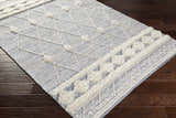 Close up of the Moe Area Rug, a hand woven rug with a blue and cream diamond pattern and textured details. Corner