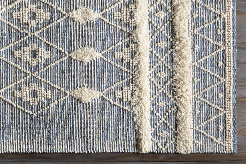 Close up of the blue and cream Moe Area Rug, featuring a geometric pattern and fringe detail. Corner