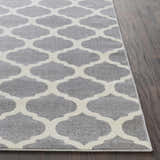 Close-up of the Mongo Carpet, a cream and slate rug with a contemporary quatrefoil pattern on dark wood flooring. Front