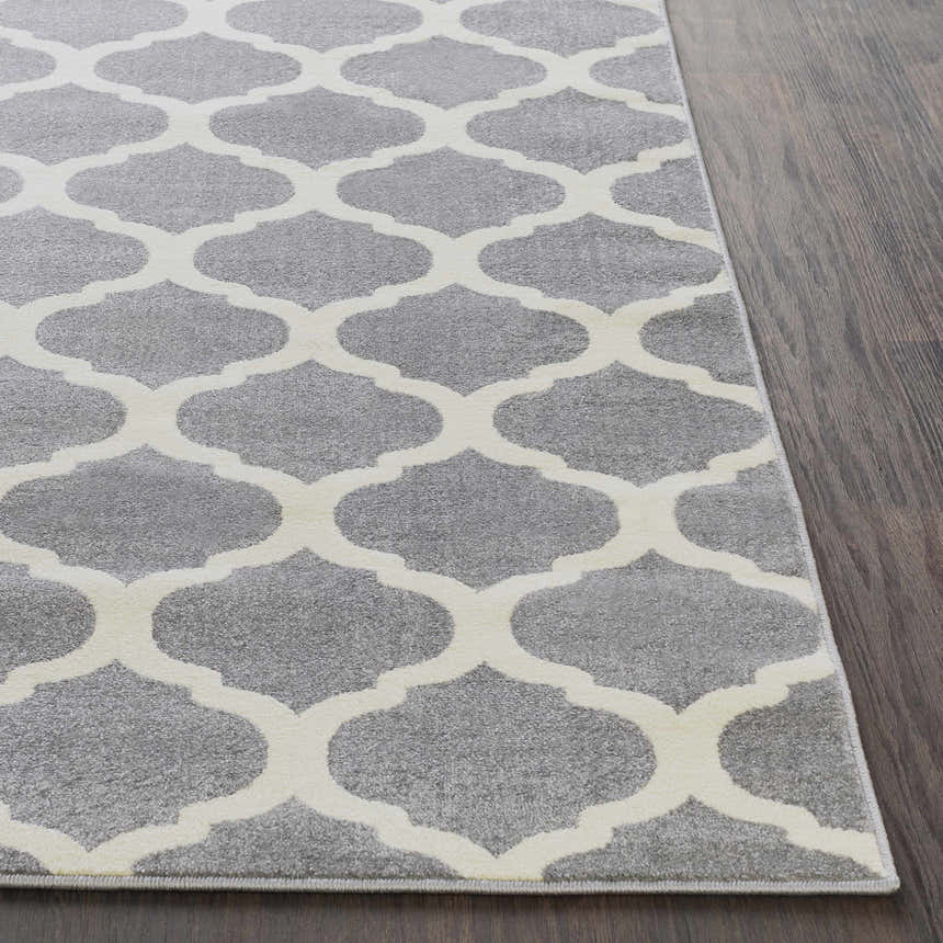 Close-up of the Mongo Carpet, a cream and slate rug with a contemporary quatrefoil pattern on dark wood flooring. Front