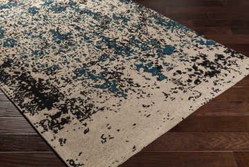 Close-up of the Sweeny Teal Abstract Area Rug showing beige, black, and teal abstract pattern on dark wood floors. Corner