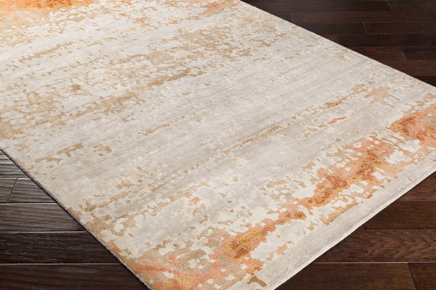 Close up of Mossyrock Premium Rug. Contemporary design in brick red, camel, cream, and tan on dark wood floor. Corner