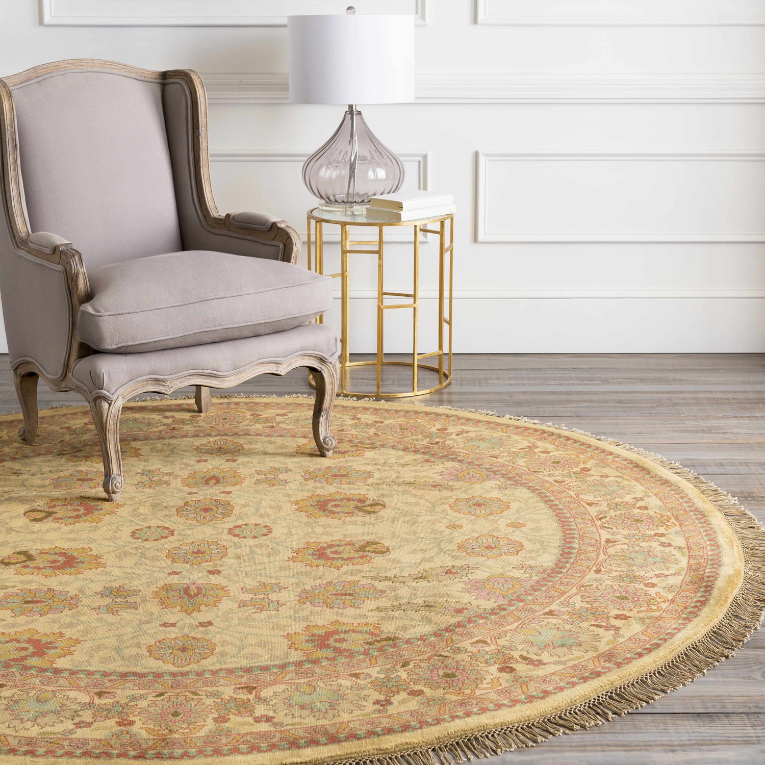 Living room scene with a round Maurice Area Rug in brick red, brown, and mustard under a gray chair and gold side table. Roomscene-Round
