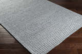 Close-up of the hand woven Mulgoa Area Rug in medium gray, showing its textured, contemporary design on dark wood floors. Corner