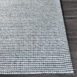 Close-up of the textured, hand-woven Mulgoa Area Rug. Medium gray wool and polyester rug on dark wood floor. Front