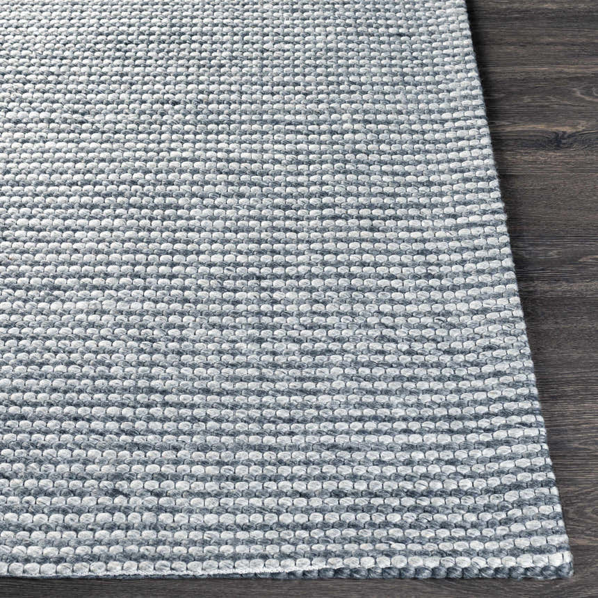 Close-up of the textured, hand-woven Mulgoa Area Rug. Medium gray wool and polyester rug on dark wood floor. Front