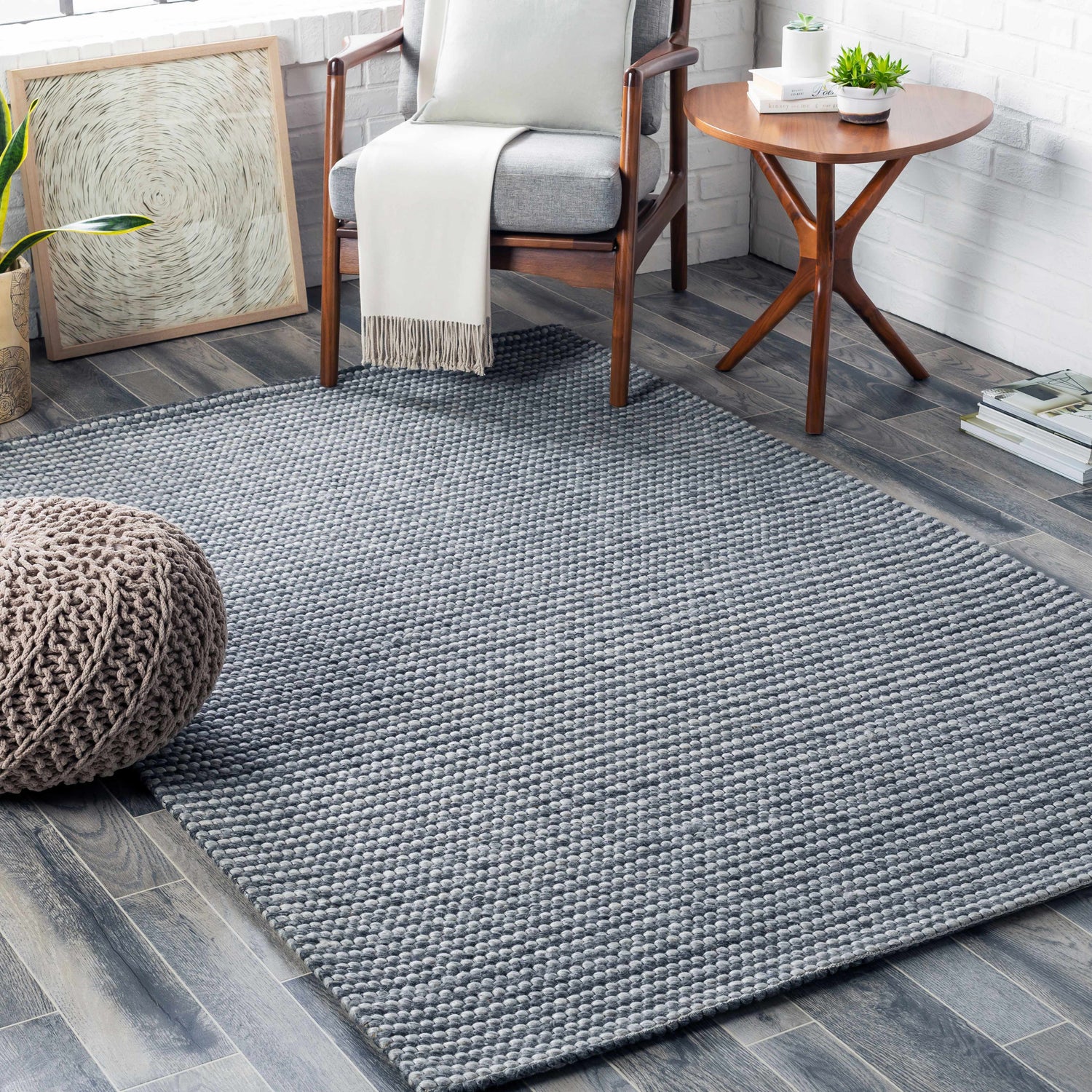 Living room scene with a medium gray Mulgoa Area Rug, gray chair, wood side table, and a knit pouf. Roomscene-Rectangle