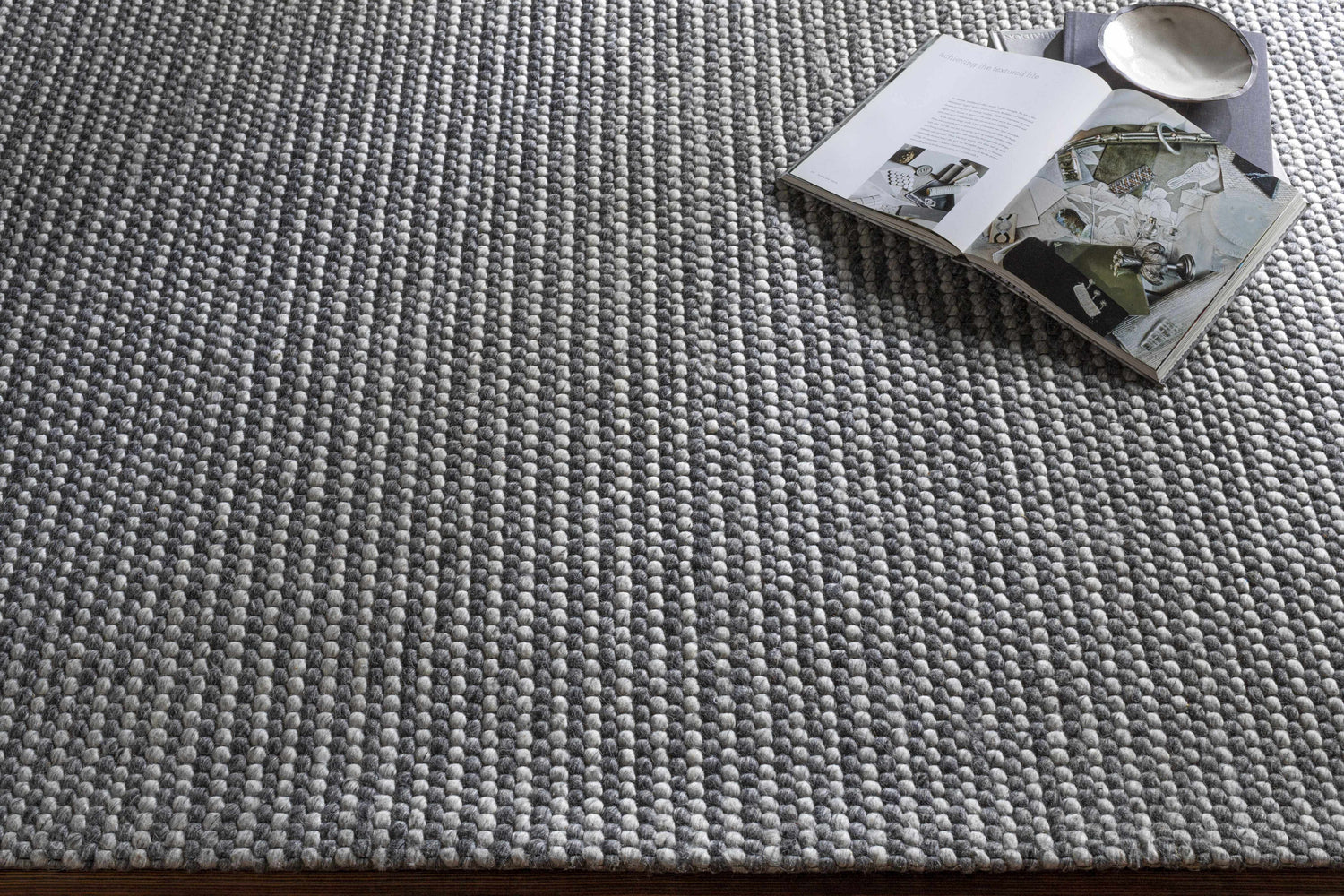 Close-up of the hand woven Mulgoa Area Rug. Medium gray rug with a contemporary design and textured wool and polyester feel. Styleshot