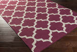 Close-up of Muskogee Hand Woven Magenta Lattice Rug showing magenta and ivory quatrefoil pattern on dark hardwood floor. Corner