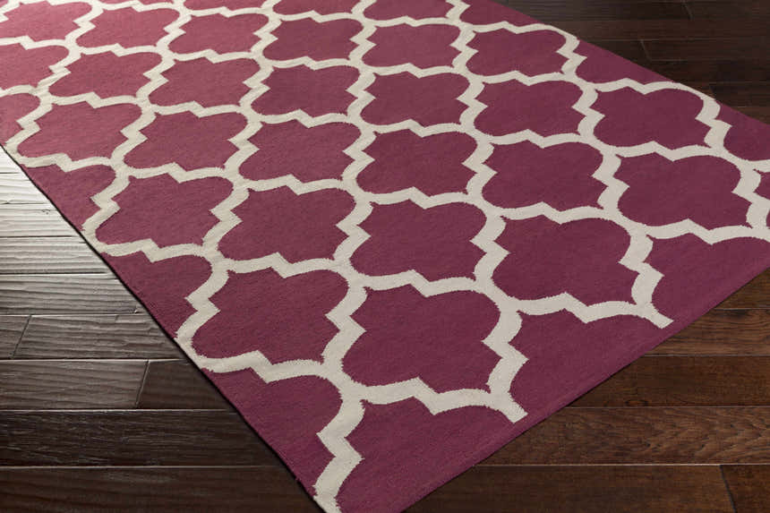 Close-up of Muskogee Hand Woven Magenta Lattice Rug showing magenta and ivory quatrefoil pattern on dark hardwood floor. Corner
