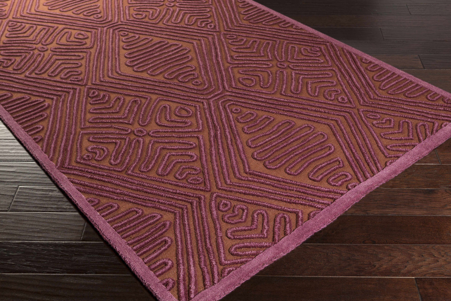Close-up of the hand woven Mylo Area Rug. Burnt orange wool rug with mauve geometric pattern and border. Corner