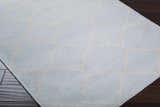 Close up of the hand woven Nadeau Area Rug. Pale blue wool with a tan geometric pattern. Corner