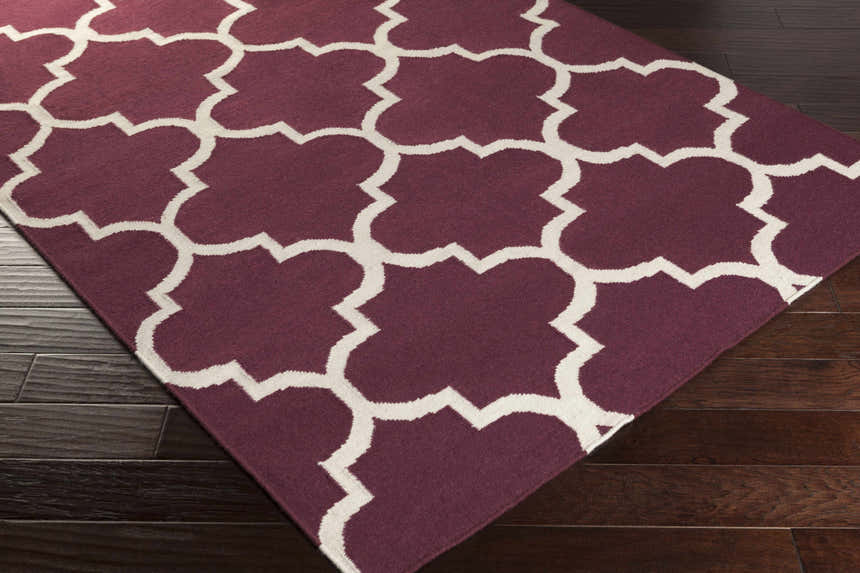 Close-up of the Nassau Area Rug, a hand woven wool rug in dark purple and ivory quatrefoil pattern on a wood floor. Corner